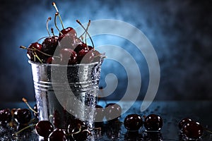 Red sweet cherries close up in a metal bucket on a dark and blue background. Summer taste.