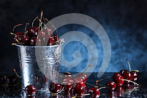 Red sweet cherries close up in a metal bucket on a dark and blue background. Summer taste.