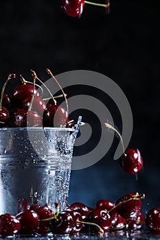 Red sweet cherries in a metal bucket on a dark and blue background. Summer taste. Fresh berries under the water drops.