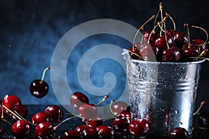 Red sweet cherries in a metal bucket on a dark and blue background. Summer taste. Fresh berries under the water drops.