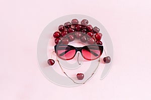 Red sweet cherry laid out in image of woman in sunglasses with lips on pink background. Concept youth, beauty, healthy eating or