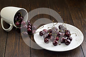 Red sweet cherry in a white plate and on dark wooden table close-up.