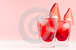 Red sweet cold party drinks in two elegant shot glasses with ice cubes, strawberry slice on pastel soft pink color background.