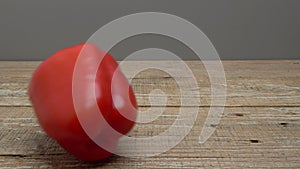 Red sweet pepper rolling on a wooden surface on a gray background. Video.