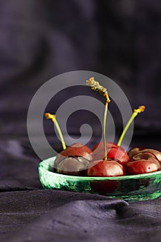 Red sweetheart cherries (grown in England) in a rustic glass bowl on a blue silk background with copy space. Selective focus.