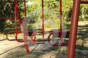 Red swings in city park in bright sunny morning