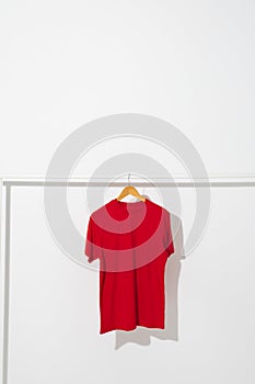 Red t shirt on hanger hanging from clothes rail with copy space on white background