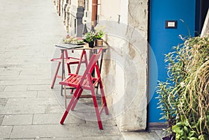 Red table and chair in an outdoor cafÃ© with blue wooden door in Syracuse Siracusa Sicily