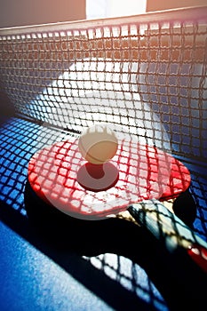 A red table tennis racket and a white ball lie on the surface of the table next to the net. Sports game