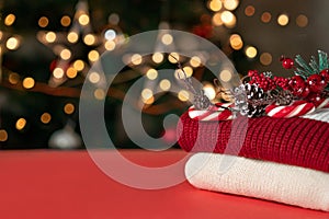 Red tabletop with empty copy space, red and white knitted sweaters, pine tree branch decoration, candy cane, blurred