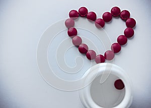 The red tablets are arranged in the shape of a heart. Red heart pills with a plastic jar.