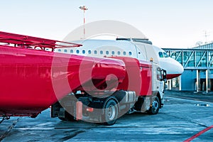 The red tanker refueling the aircraft parked to a boarding bridge at the airport apron