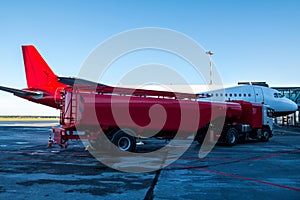 The red tanker refueling the plane parked to a boarding bridge at the airport apron