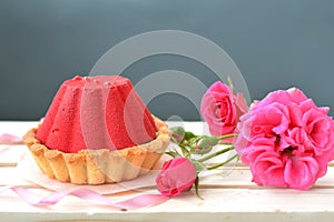 Red, tasty cake with chocolate filling and rose bush on grey background