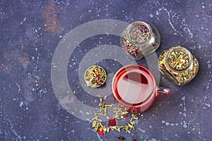 Red tea rooibos, hibiscus, karkade in glass cup and jars of dry tea leaf and petals on dark background. Herbal, vitamin, detox