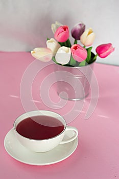 Red tea in a white mug on a pink background. Nearby is a bucket of tulips and berries