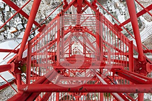 Red telecommunication tower or mast with microwave, radio panel antennas, outdoor remote radio units, power cables, coaxial cables