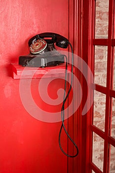 Red Telephone booth in English style. British phone box with black retro telephone standing in it.