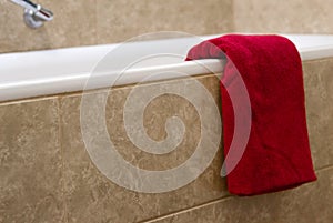Red terry bath towel is on bath with beige tiles