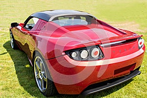 Red Tesla Roadster Sports Car Rear Side in Green Field