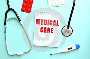 The red text MEDICAL CARE is written on a white notepad that lies next to the stethoscope on a blue background.