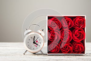 Red textured roses and alarm clock close-up and copy space. Women`s day, mother`s day, red roses and a clock on a white wooden bac