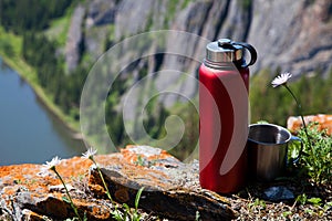 A red thermos and a mug on top of a mountain.