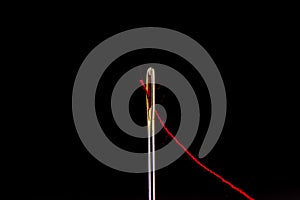 Red thread in the eye of a needle isolated on a black background.