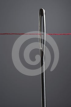 Red thread going through needle eye close-up
