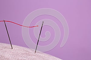 Red thread for sewing is threaded into the eye of the needle and directed to the eye of the second needle