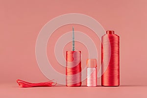 Red thread spools, needle, and bobbin on pink background