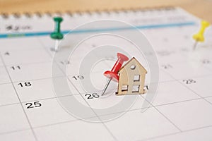 red thumbtack with miniature wooden house on calendar