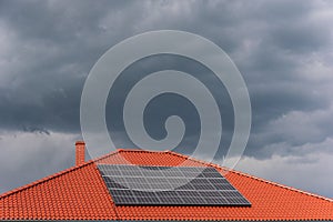 Red tile roof with photovoltaic panels during stormy weather . Solar PV installation and dark blue threatening sky