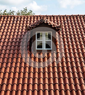 Red tiled roof with attic. Dormer window white color on garret, rooftop