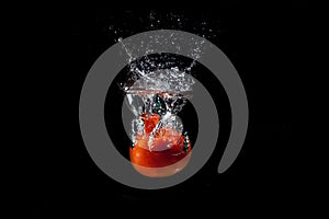 A red tomato on a black background falls into the water