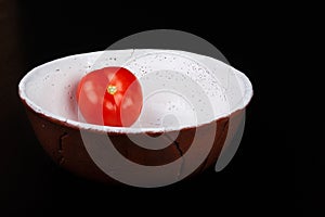 Red tomato on the ceramic bowl prepared for salad