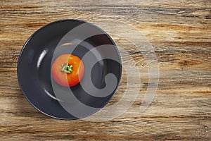 Red tomato in dark bowl cup on isolated wooden textured background