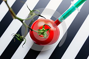 Red tomato with green stem on a striped black and white background stabbed with medical syringe photo