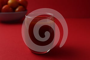 Red tomato juice in a glass next to tomatoes lie on a plate on a red background with a place for text. Healthy Food Drinks