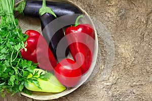 Red tomato, pepper, parsley, eggplant lie on a wooden plate on a brown background