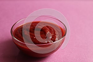 Red tomato sauce in a glass sauce bowl stands on a pink fuchsia background with a copy space