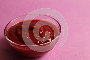 Red tomato sauce in a glass sauce bowl stands on a pink fuchsia background with a copy space