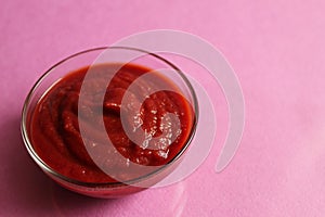 Red tomato sauce in a glass sauce bowl stands on a pink fuchsia background with a copy space