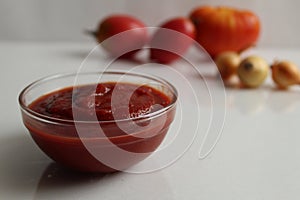 Red tomato sauce ketchup in a glass salad bowl saucepan on a white background are vegetables in the background red tomatoes