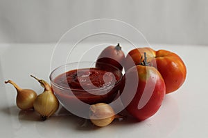 Red tomato sauce ketchup in a glass salad bowl saucepan on a white background are vegetables in the background red tomatoes