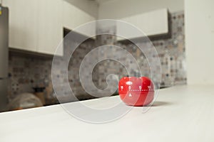 Red tomato-shaped kitchen timer with cooking in the background.