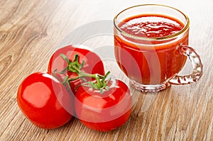 Red tomatoes on branch, cup of tomato juice on wooden table