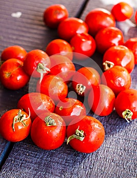 Red tomatoes cherry on dark wooden board, vertically