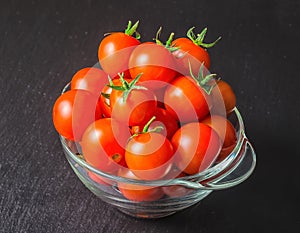 Red tomatoes cherry in transparent salad bowl on black