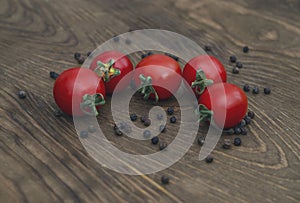 Red tomatoes and dry black pepper on a wooden background